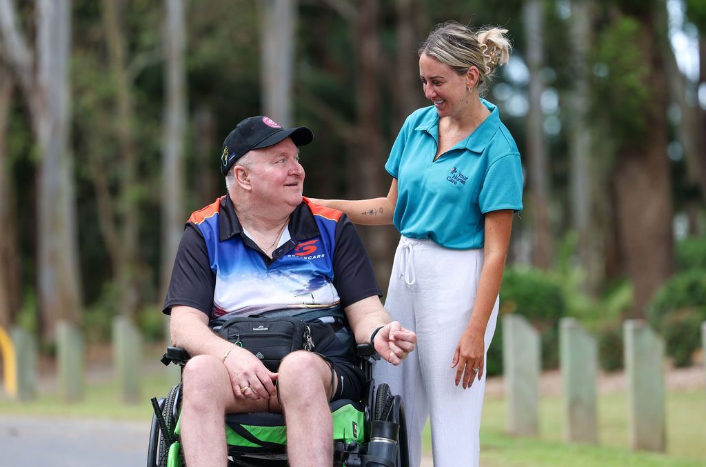 A home care provider supports a man in a wheelchair, offering compassionate care.